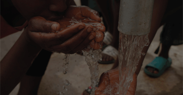 Close-up van handen die water drinken uit een waterpomp, als illustratie van het risico op buiktyfus door besmet drinkwater.