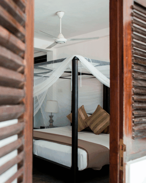 Hotelkamer met een hemelbed en een opgehangen klamboe, gezien door een houten luik.