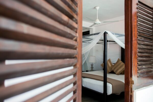 Hotelkamer met een hemelbed en een opgehangen klamboe, gezien door een houten luik.